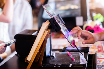 Selective focus to edge of the tablet with blurry cashier staff using tablet to receive orders from customers at counter service in cafe or store.