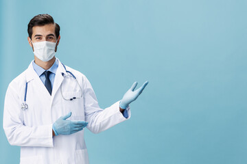 Male doctor in a white coat and medical mask shows hand gestures and looks at the camera on a blue...