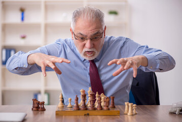 Old businessman employee playing chess at workplace