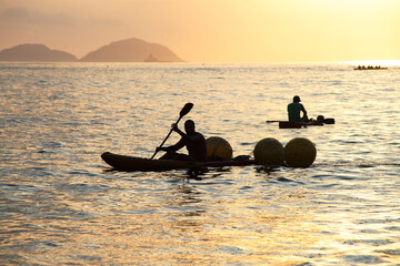 silhouettes of people in canoes at dawn on Copacabana beach in Rio de Janeiro.