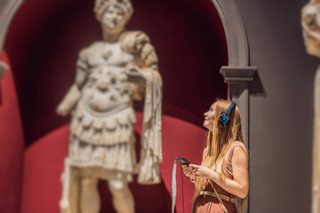Portrait of contemporary young woman looking at sculptures and listening to audio guide at museum exhibition