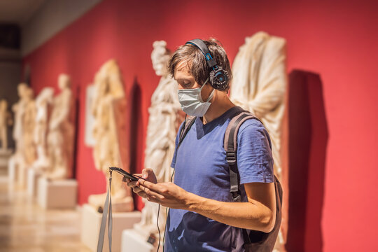 Portrait of contemporary man looking at sculptures and listening to audio guide at museum exhibition