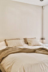a bed with pillows and blankets on it in a room that has white walls, wood flooring and large windows