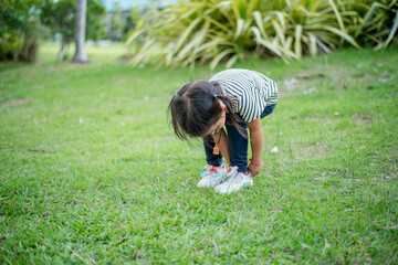 Asian girl bends down to put on shoes by herself in the backyard while doing mom and dad family vacation activities.