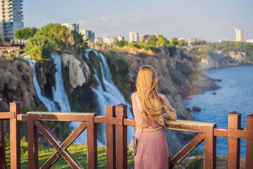 Naklejka premium Beautiful woman with long hair on the background of Duden waterfall in Antalya. Famous places of Turkey. Lower Duden Falls drop off a rocky cliff falling from about 40 m into the Mediterranean Sea in