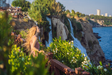 Naklejka premium Beautiful woman with long hair on the background of Duden waterfall in Antalya. Famous places of Turkey. Lower Duden Falls drop off a rocky cliff falling from about 40 m into the Mediterranean Sea in