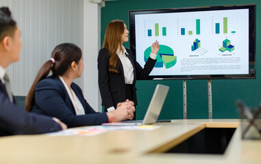 Asian professional successful smart confident female businesswoman presenter lecturer in formal business suit standing presenting graph chart document information on computer screen in meeting room