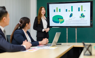 Asian professional successful smart confident female businesswoman presenter lecturer in formal business suit standing presenting graph chart document information on computer screen in meeting room