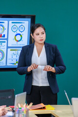 Millennial Asian professional successful female businesswoman lecturer presenter in formal business suit standing pointing computer monitor presenting graph chart financial info to businessman client
