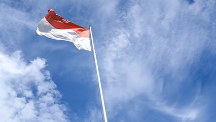 
Low angle view of Indonesian National Flag, Merah Putih, under cloudy blue sky. The flag consists of red and white colors symbolizing the color of blood and bones of its people. National Independence