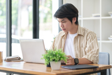 Young asian man entrepreneur dressed smart casual working on laptop while sitting in modern workplace.