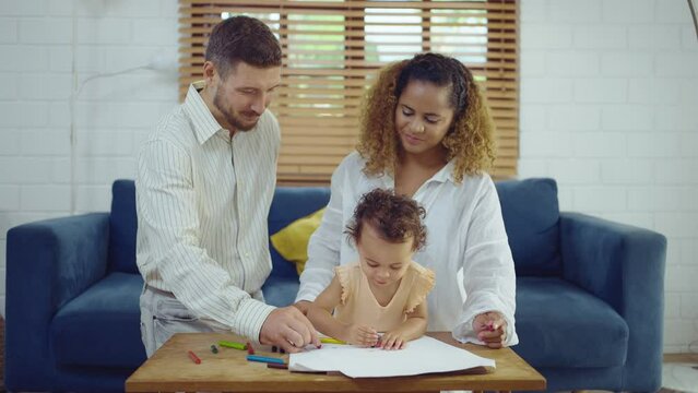 Dad, Mom and little daughter drawing with colorful pencils on paper happy smiling.Young family spend free time together in living room at home.