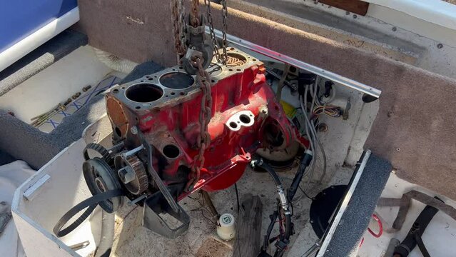 An onboard 4 cylinder engine block is slowly lifted from a boat with a chain and hoist