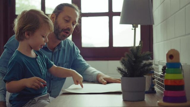 Caucasian family painting on paper with son indoors in house. Little son learn how to draw art picture enjoy creativity with father in house.