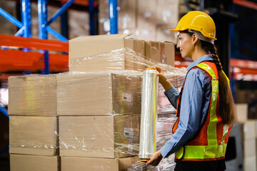 Female worker wrapped a parcel of stretch film on a cargo in a large factory warehouse. Logistics...