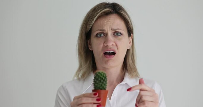 A young woman touches a cactus, a close-up. Pain of plant spike, slowmotion, negative emotions