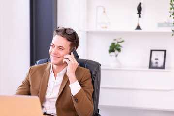 Businessman in brown suit color using mobile phone in modern office