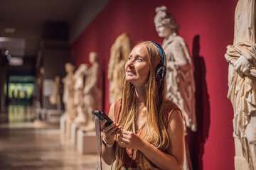 Portrait of contemporary young woman looking at sculptures and listening to audio guide at museum exhibition - obrazy, fototapety, plakaty