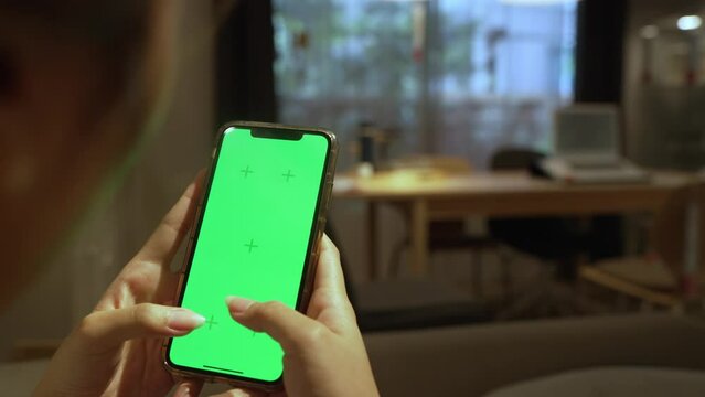 Person living room holding in hands a smartphone with green screen chroma mock up over a comfy blurred living room background