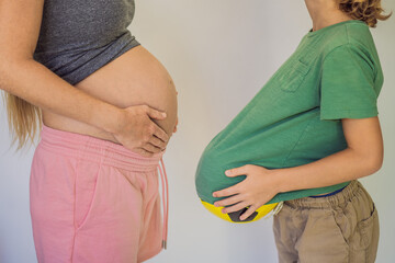 Amusing son. Pregnant beautiful woman amusing her little son while putting yellow ball under his green shirt
