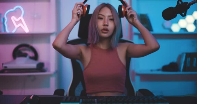 Footage of Young Asian female esports gamer sitting in chair facing back and looking at camera with neon lights at home. Female gamers are enjoying the technology of live streaming.