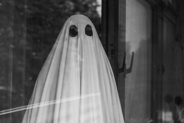 Sad ghost in white sheet outside the window of an abandoned house
