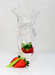 Strawberry fruit drops onto a wine glass, freeze motion of the water splash, white background.