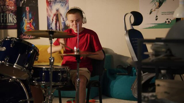 Adult man plays on traditional djembe drum at home. Camera changes view to neighbour boy in headphones practicing musician skills using drum kit. Apartments separated by wall. Neighbourhood. Whip pan.