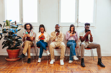 Five young people using phones while sitting together in room.