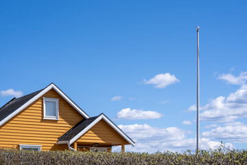 Norwegian landscape with a green hedge behind a yellow wooden building facade with a white window,...