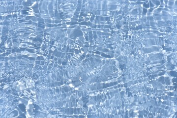 Blue water with ripples on the surface. Defocus blurred transparent blue colored clear calm water surface texture with splashes and bubbles. Water waves with shining pattern texture background.