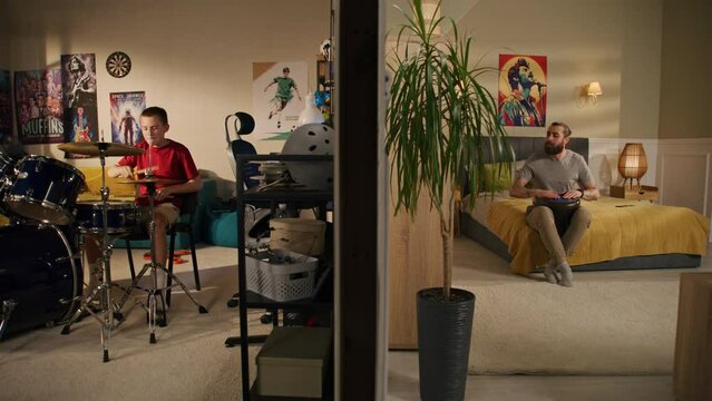Young boy plays drum kit in bedroom. Male musician plays traditional djembe drum at home. View of two rooms or apartments separated by wall. Low level of sound insulation. Concept of neighbourhood.