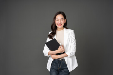 Asian female executive with long hair cute smile holding tablet and pen for work crossed arms, powerful posture Wearing a white suit, jeans and standing in a gray studio setting - obrazy, fototapety, plakaty