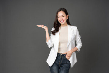 Asian female executive with long hair confident smile Wear a white suit, jeans and raise your right hand to present. left hand in trouser pocket The photo was taken in a gray background studio.