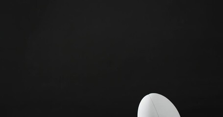 White rugby ball on kicking tee on sunlit grass and black background with copy space, slow motion