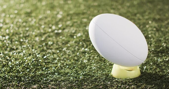 White rugby ball on kicking tee on sunlit grass with copy space, slow motion