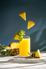 pineapple juice in a glass on a blue and white  background with reflection, fresh fruit splashes and levitation. High quality photo, conceptual art, copy space
