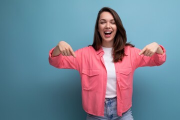 cheerful brunette lady in a pink shirt and jeans points her finger at the infomation on a studio background