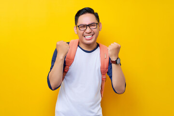 Excited young Asian man student wearing t-shirt with backpack making winner gesture and celebrating...