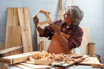 Happy senior carpenter with finished work, woodworking shop business owner