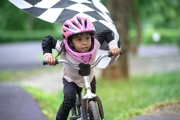 4 years old girl with helmets practicing balance bike, little girl have fun at the pump track, riding  through black and white crossed Checkered flag, kids with outdoor sports