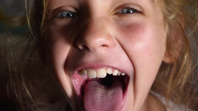 Blue-eyed girl showing teeth, tongue, and soft palate wide open mouth. The tongue is far out. Close-up