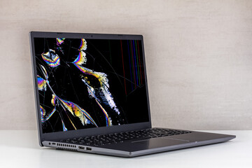laptop pc with a broken screen in cracks and with leaking crystals on a gray background close up