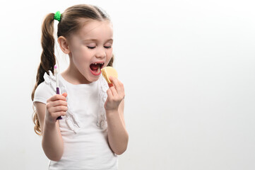 little girl bites potato chips and holds toothbrush on white background.