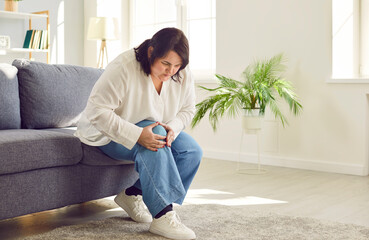 Portrait of young plus size overweight woman holding a knee suffering from osteoarthritis or...