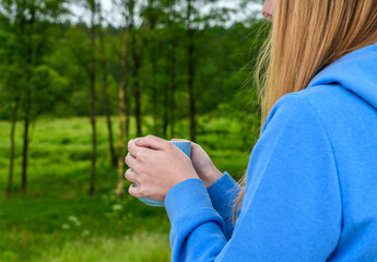 Kobieta w lesie trzymająca w dłoniach kubek z ciepłym napojem - obrazy, fototapety, plakaty