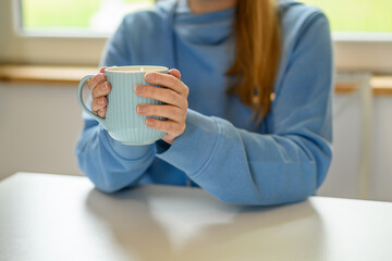 Kobieta siedząca przy stole trzymająca w dłoniach kubek z kawą  - obrazy, fototapety, plakaty