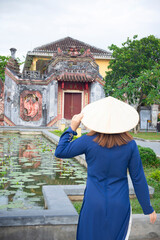 Asian woman is wearing Ao Dai traditional Vietnamese dress and traveling at the Ba Mu Temple Gate, Hoi an old town in Vietnam. The Chinese text translates "the centre gate"