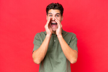 Young caucasian handsome man isolated on red background shouting and announcing something