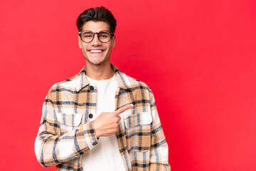 Young caucasian handsome man isolated on red background pointing to the side to present a product